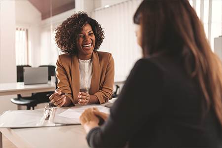 smiling female business owner sitting at desk with female banker talking about business credit cards